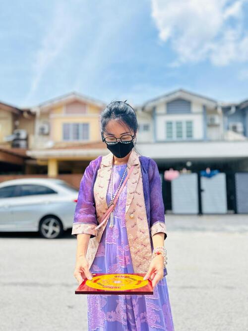 Master-Maggie-Zhu-朱一心-16 (1) Master Yixin conducting a Feng Shui assessment outside a residential home, holding a Luo Pan compass to analyse property orientation under bright daylight.