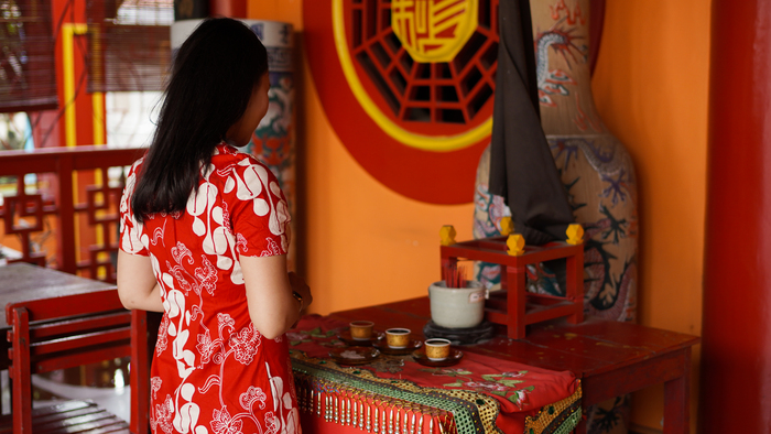 Woman in a red dress offering prayers at a traditional altar, reflecting on her BaZi analysis in Singapore to align with positive energy and life cycles.