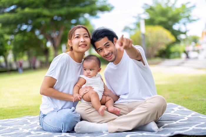 Happy young family sitting outdoors with their baby, symbolising harmony and balance achieved through Feng Shui baby naming and BaZi guidance.